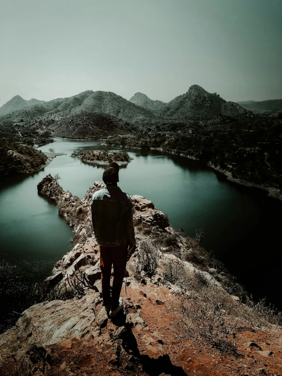 man standing at the top of a mountain overlooking a lake