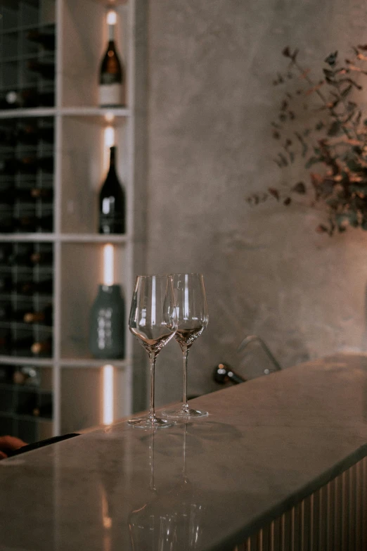 a couple of wine glasses sitting on top of a counter, from the distance, with a figure in the background