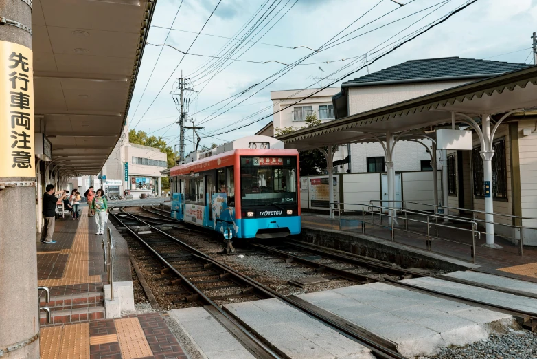 a blue and red train pulling into a train station, unsplash, sōsaku hanga, square, street of teal stone, brown, tram