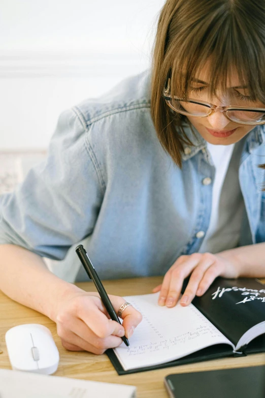 a girl wearing glasses is writing in an exercise book