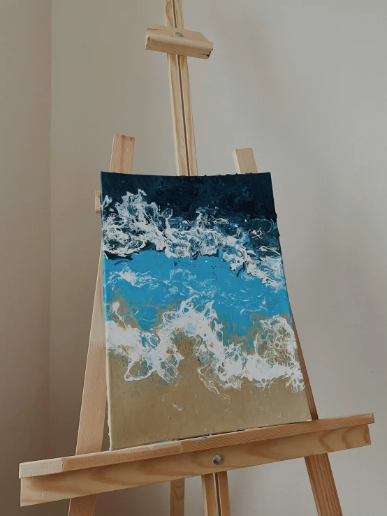 a close up of an easel with a painting on it, an acrylic painting, inspired by Katsushika Hokusai, unsplash, abstract art, foamy waves, gold and blue, on a white table, portrait of small