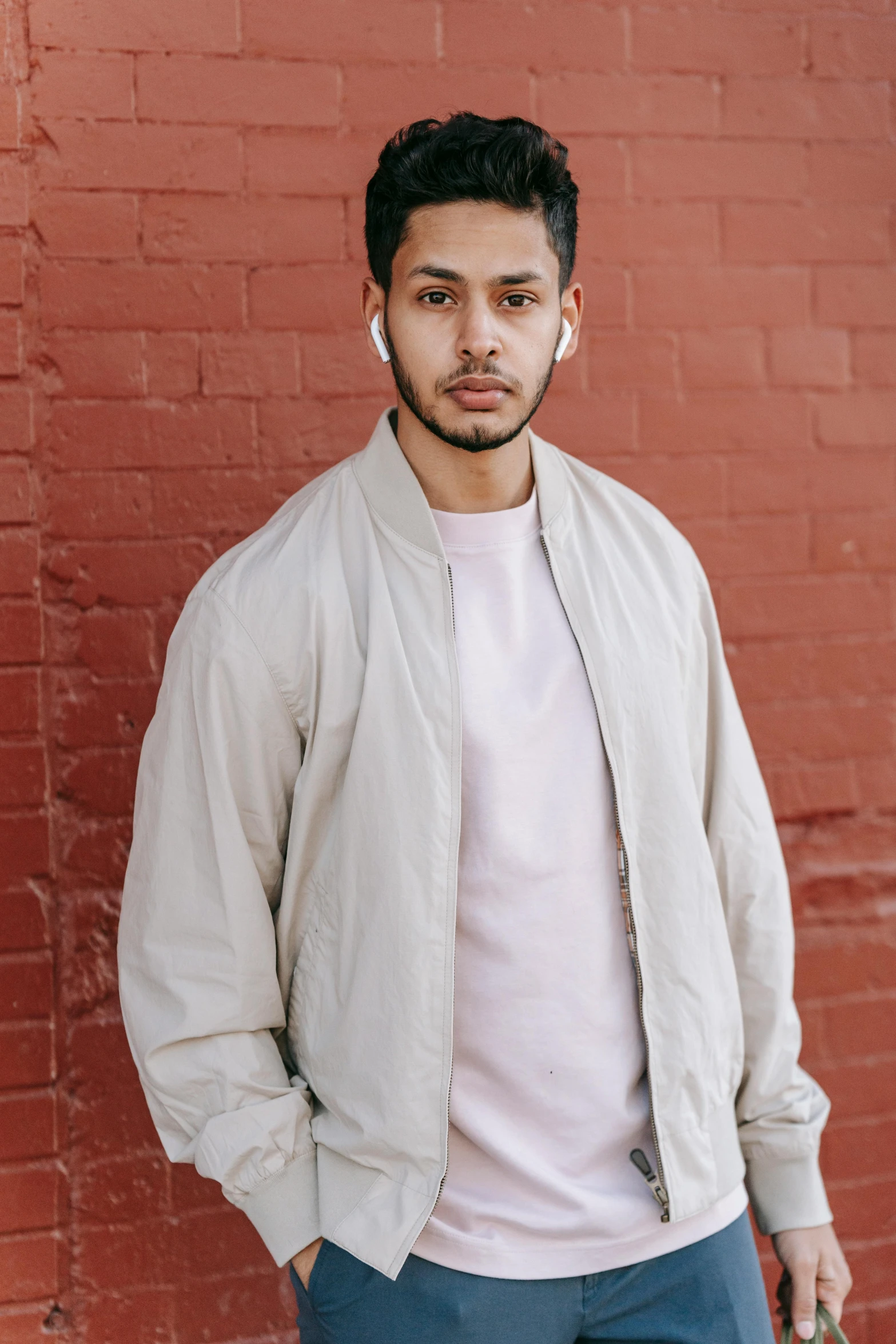 a man standing in front of a brick wall, by Robbie Trevino, bomber jacket, wearing a light shirt, earbuds, ash thorp khyzyl saleem