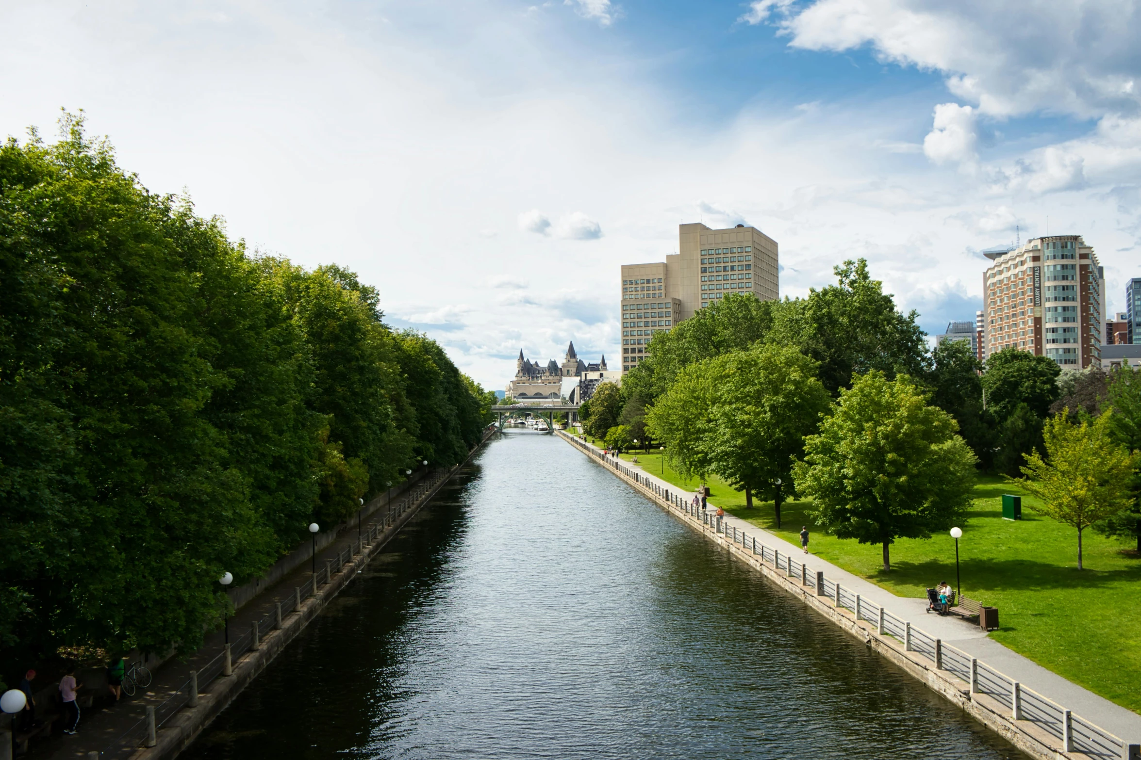 a river running through a lush green park next to tall buildings, by Julia Pishtar, quebec, parliament, river flowing through a wall, paisley