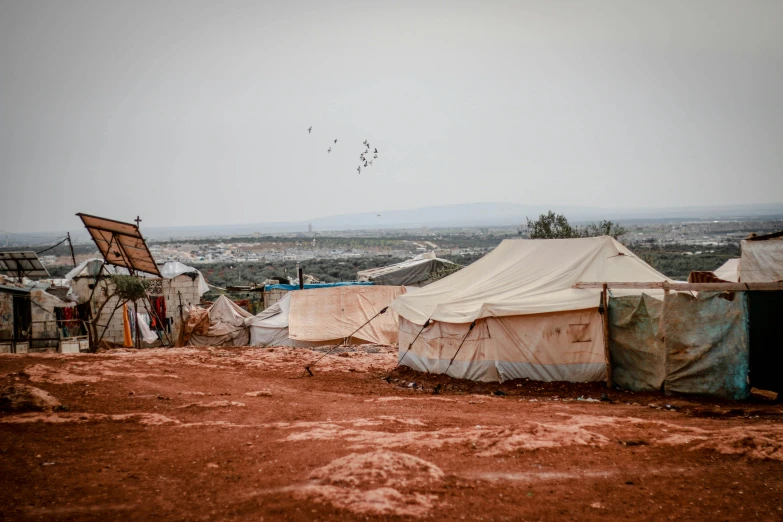 a group of tents sitting on top of a dirt field, an album cover, hurufiyya, view of villages, refugees, high quality photo, sara ali