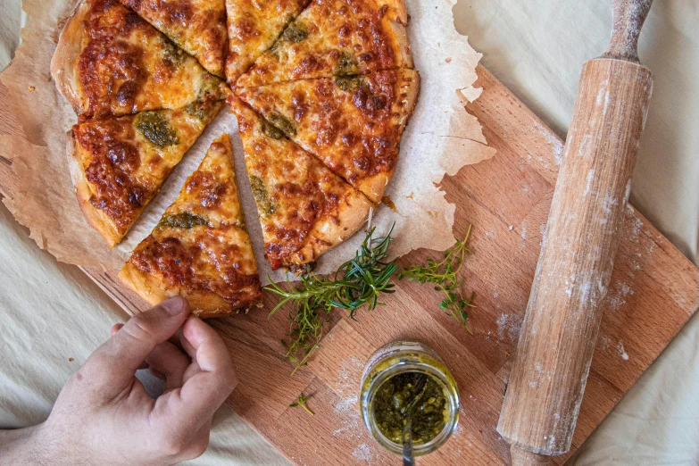 a pizza sitting on top of a wooden cutting board, a photo, inspired by Michelangelo Buonarotti, pexels contest winner, herbs, hand on table, melted cheddar, tall angle