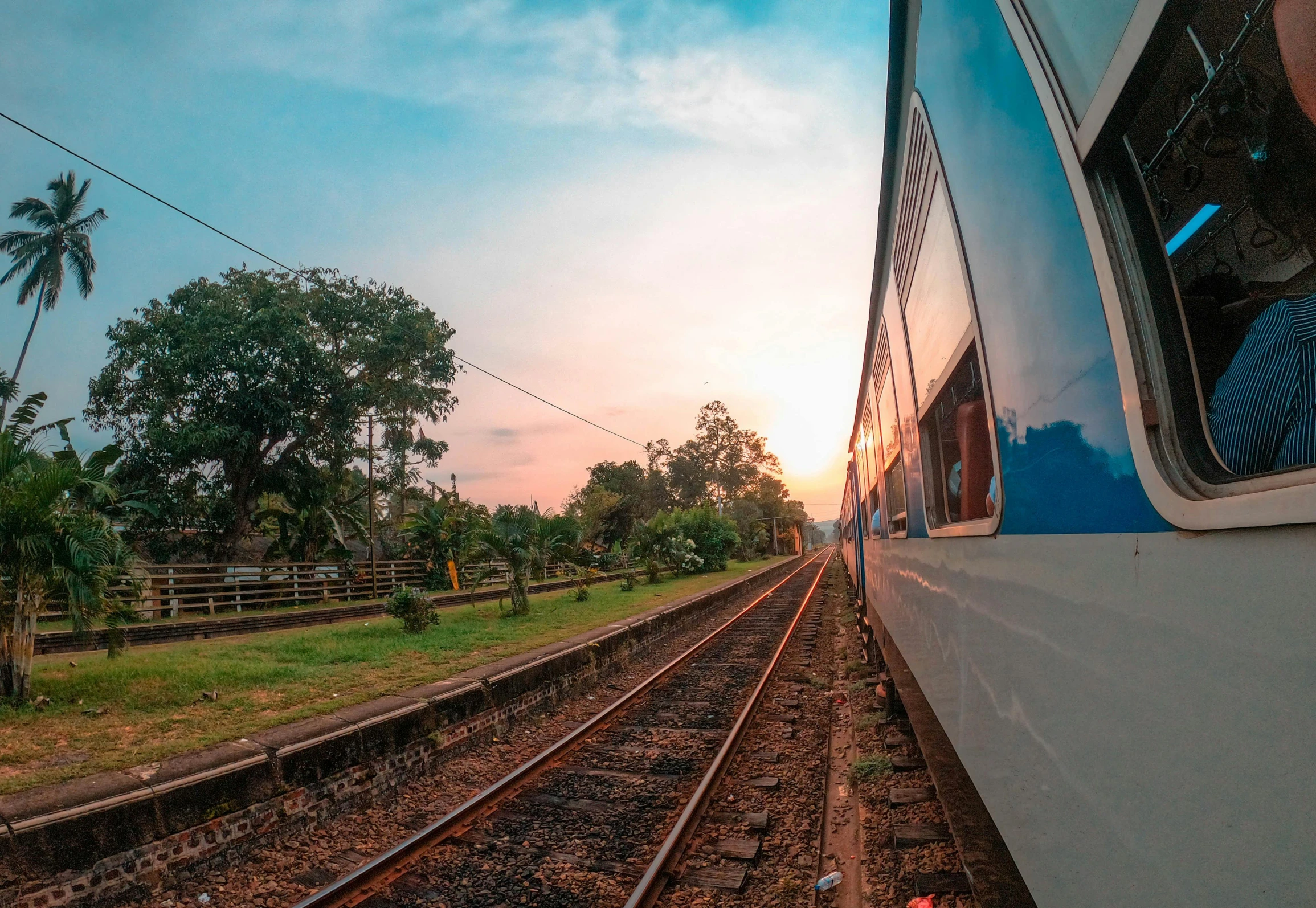 a train traveling down train tracks next to a lush green field, a picture, pexels contest winner, happening, sri lanka, sunset panorama, 🚿🗝📝