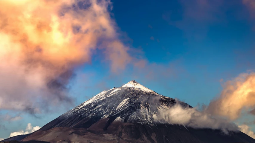 the top of a snow covered mountain with a few clouds in the sky