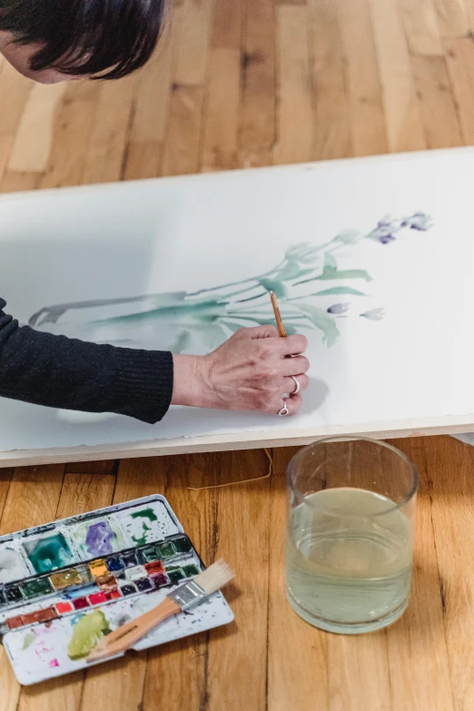 a woman is painting a picture on a piece of paper, a watercolor painting, inspired by artist, trending on pexels, botanicals, this painting is a large canvas, jenni pasanen, ultrawide watercolor