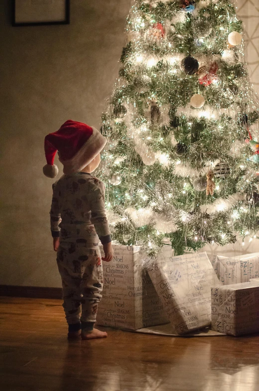 a boy stands in front of a christmas tree