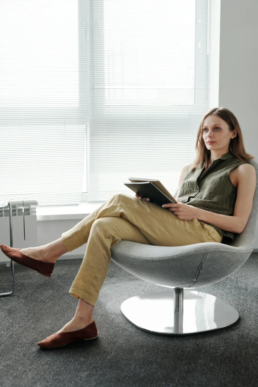 a woman sitting in a chair reading a book, wearing business casual dress, aeron alfrey, wearing pants, non binary model