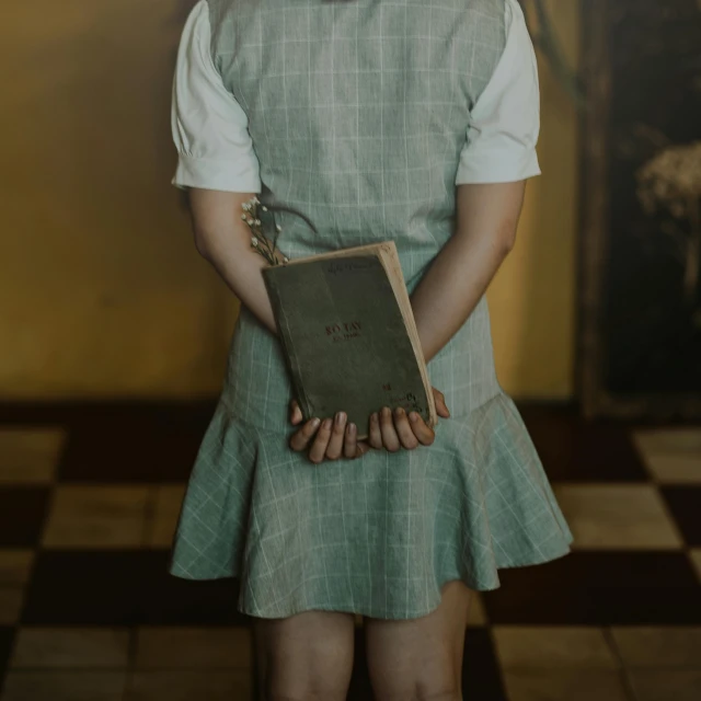 a little girl holding a book in her hands, an album cover, by Elsa Bleda, pexels contest winner, surrealism, ( waitress ) girl, desaturated, moody : : wes anderson, magical school student uniform