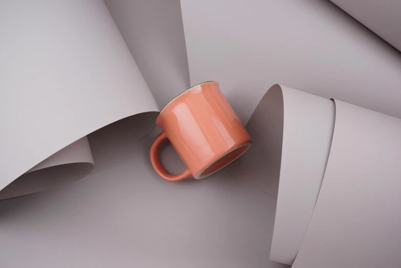 a coffee cup sitting on top of a pile of paper, a 3D render, inspired by Christo, trending on pexels, in shades of peach, mug shot, grey orange, gloss finish