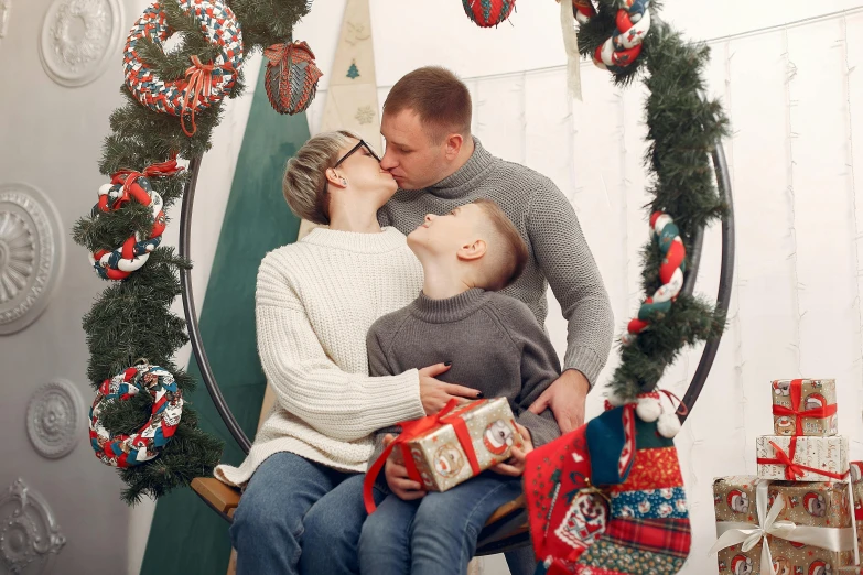 a man and woman holding a baby next to a tree with presents