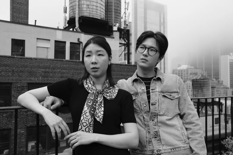 a man and a woman standing next to each other, a black and white photo, inspired by Wang Duo, sitting on a skyscraper rooftop, korean, promotional image, asian women