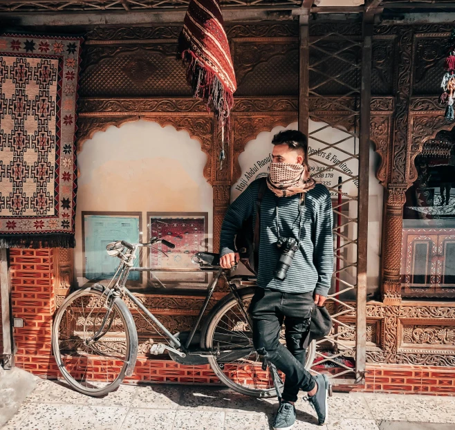 a man standing next to a bicycle in front of a building, sunglasses and a scarf, quirky shops, asian man, 🦩🪐🐞👩🏻🦳