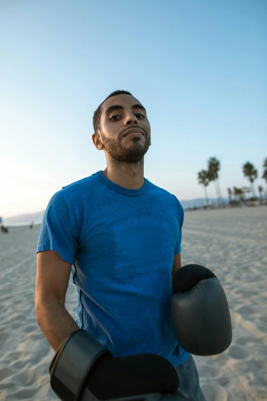 a man holding a pair of gloves and wearing a blue shirt on a beach