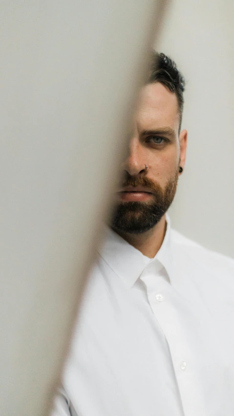 a man with black eyes and beard standing by a wall