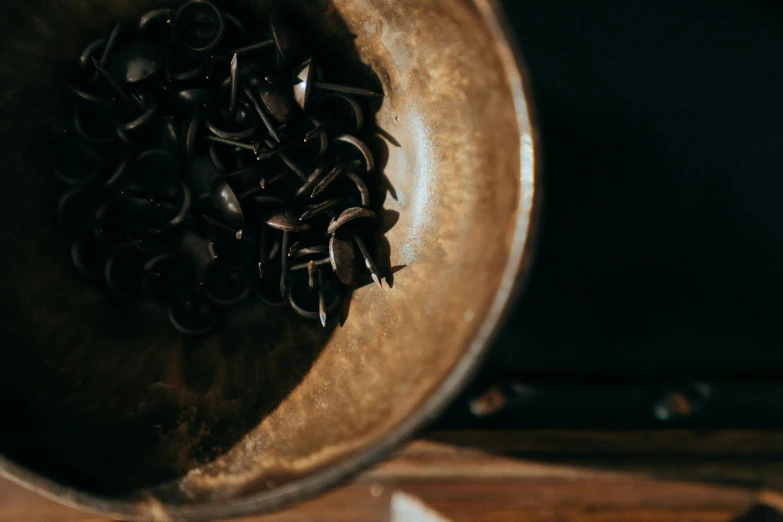 a metal bowl sitting on top of a wooden table, trending on pexels, process art, spikes on the body, black, buttons, dark brown