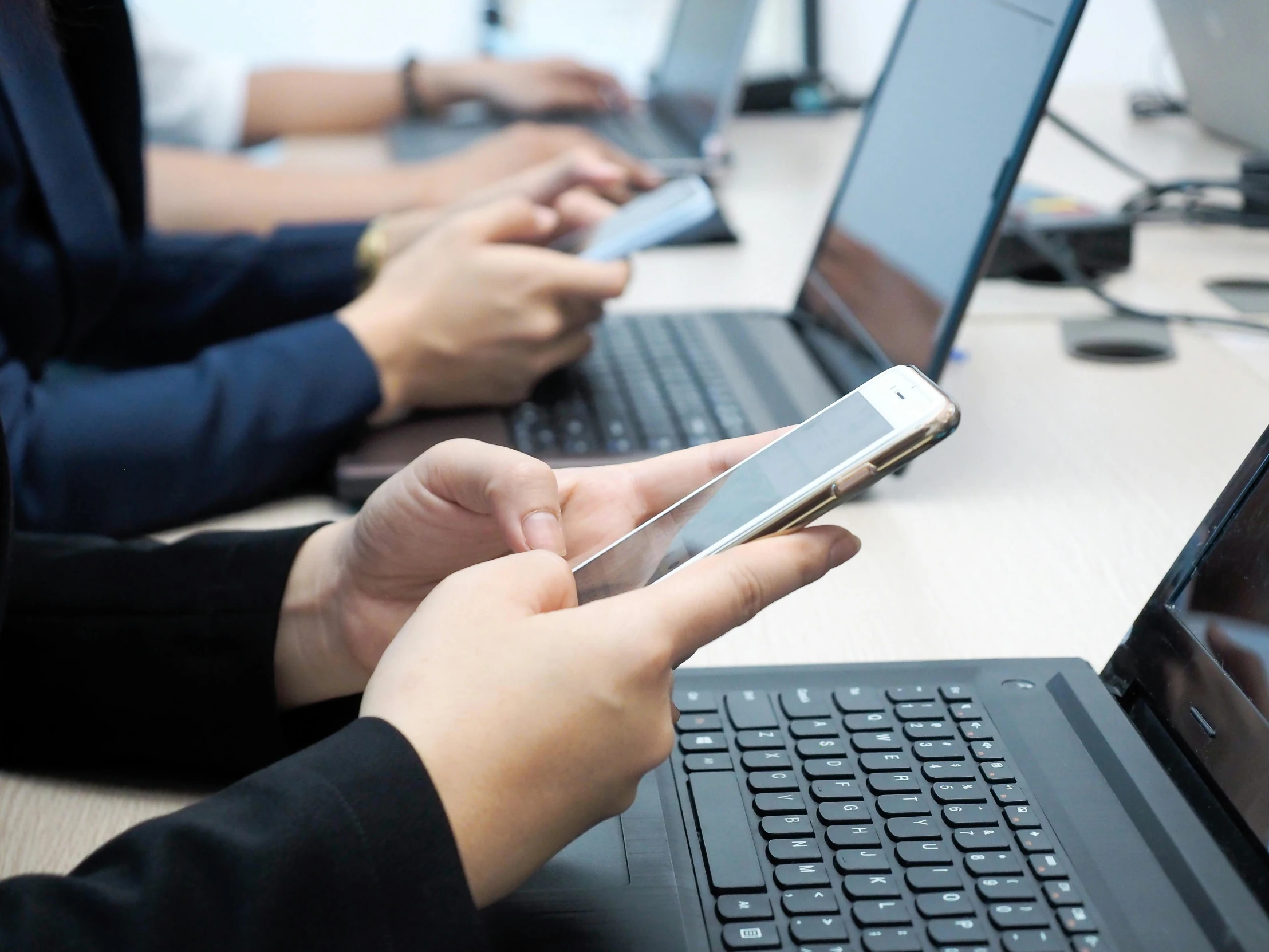 a group of people sitting at a table with laptops, by Carey Morris, shutterstock, corporate phone app icon, holding a very advance phone, link from zelda using computer, colour photo