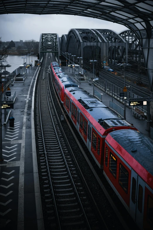 a red train traveling down train tracks next to a bridge, by Sebastian Spreng, pexels contest winner, happening, grey, subways, thumbnail, full frame image