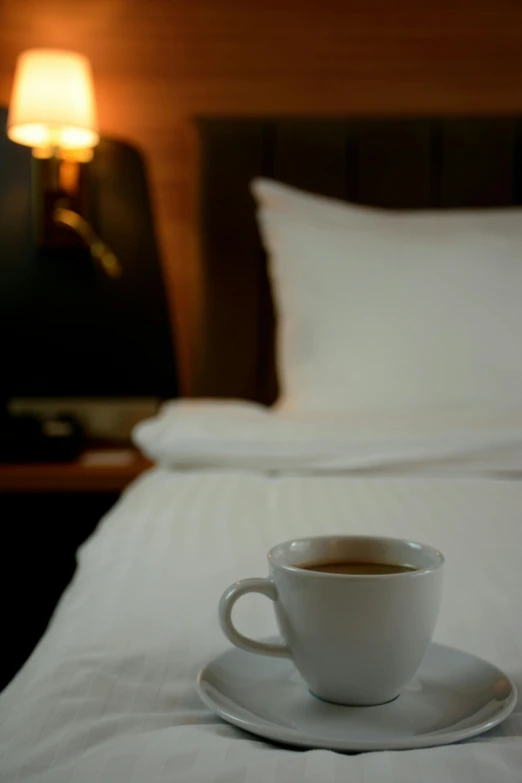 a white cup with liquid is sitting on a saucer on the bed