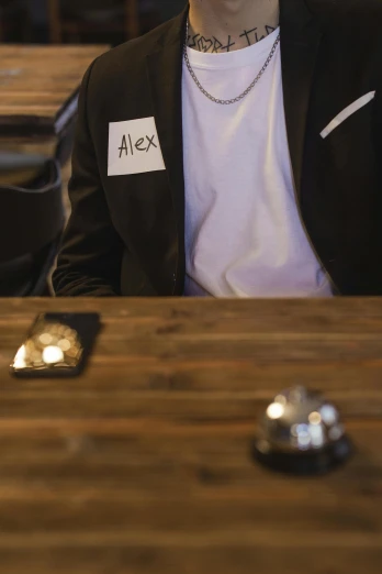 a man sitting at a table in a restaurant, an album cover, by Jessie Alexandra Dick, happening, badge on collar, shot on alexa, pair of keycards on table, no text