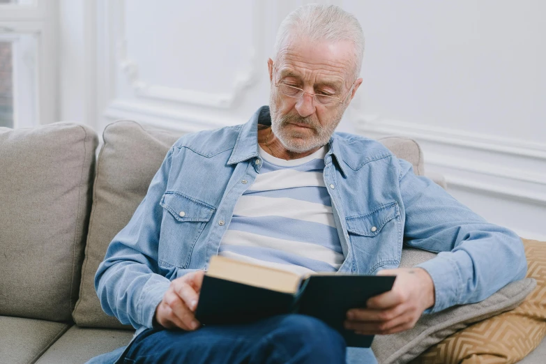 a man sitting on a couch reading a book, pexels contest winner, hyperrealism, short white beard, looking old, thumbnail, low quality photo