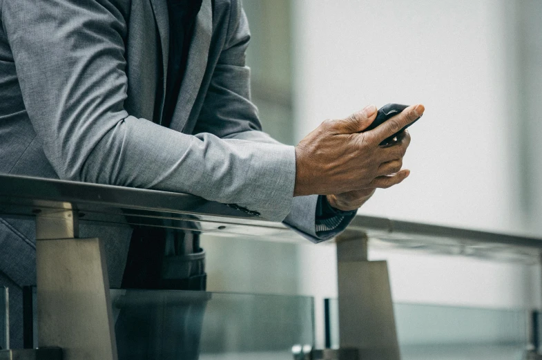 a close up of a person holding a cell phone, by Sebastian Vrancx, business clothes, thumbnail, sitting on top a table, wearing dark grey suit