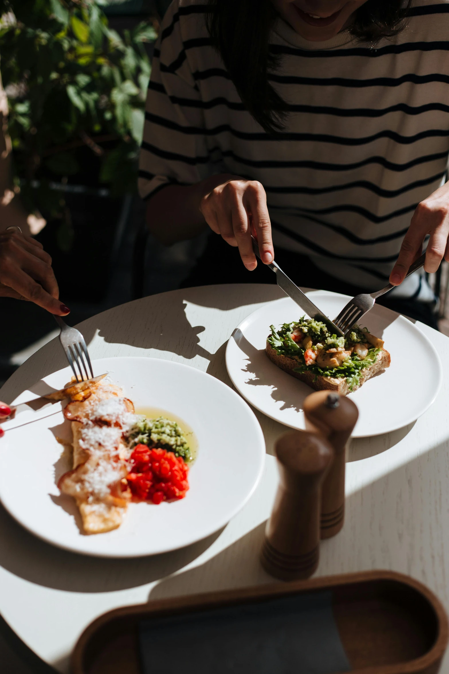 a woman sitting at a table with two plates of food, by Julia Pishtar, pexels contest winner, filleting technique, plated arm, basil gogos, male and female