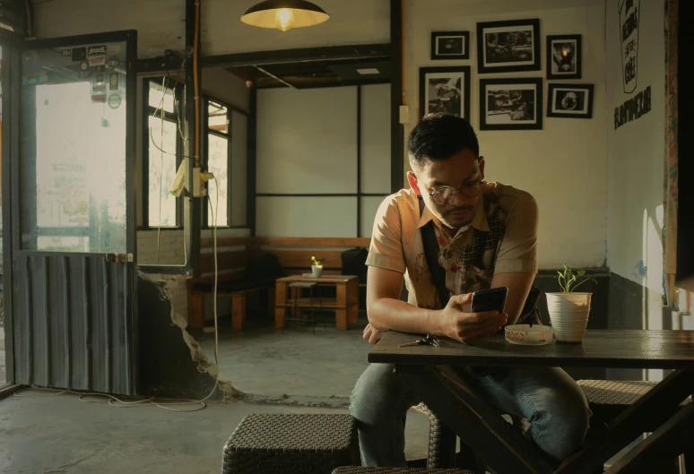 a man sitting at a table using a cell phone, inspired by Rudy Siswanto, **cinematic