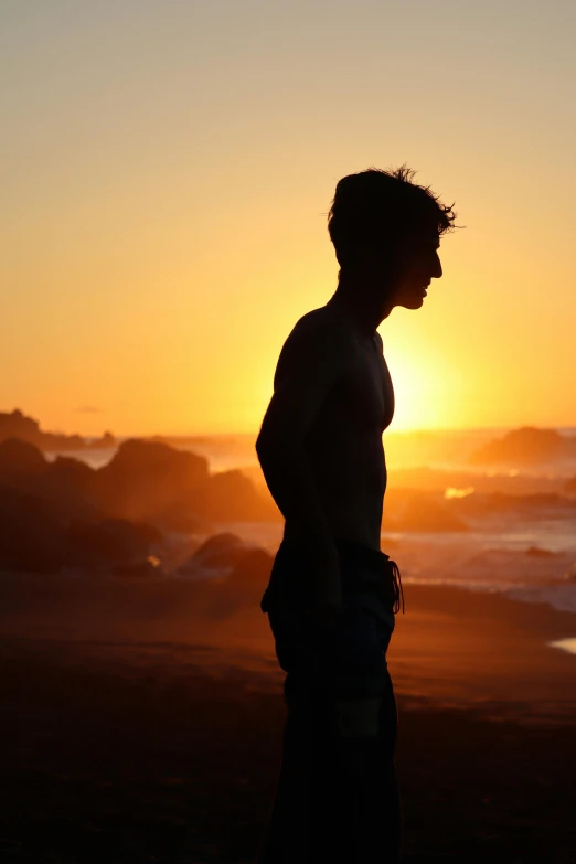 a person standing on a beach at sunset, slightly muscular, teenage boy, profile picture 1024px, siluettes