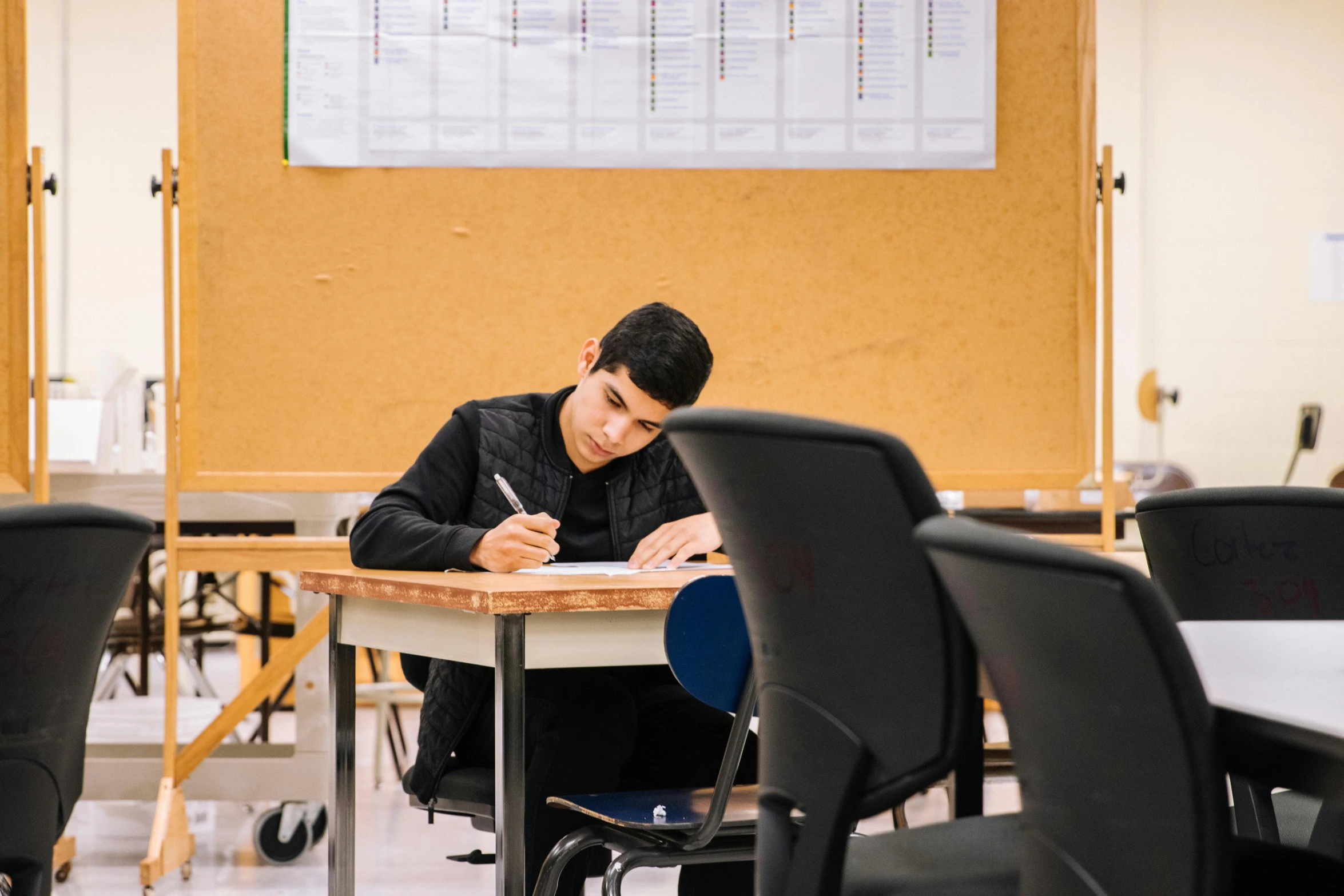 a man sitting at a desk writing on a piece of paper, by Nicolette Macnamara, pexels contest winner, academic art, classroom in background, lachlan bailey, nekro petros afshar, sitting alone