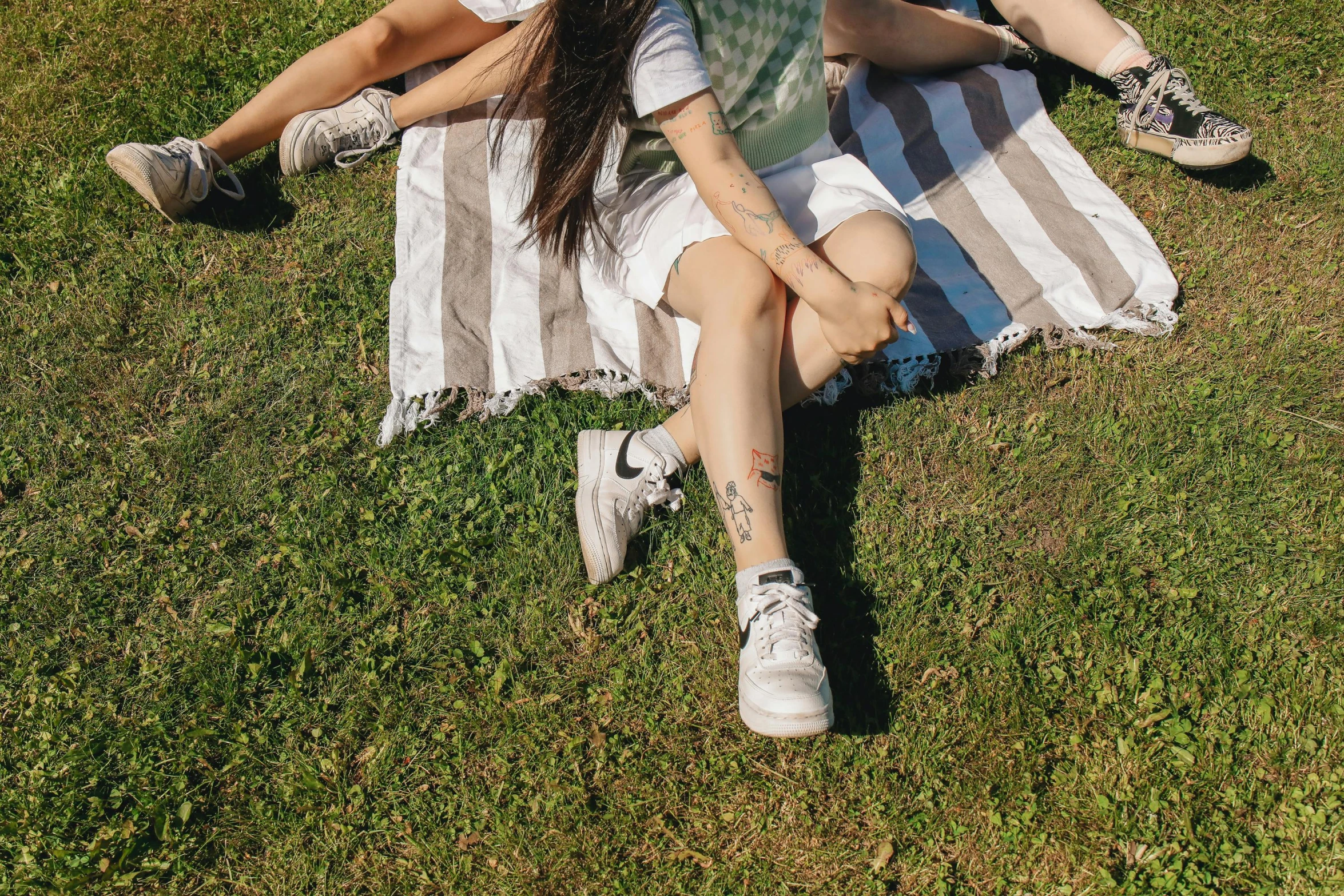 a couple of people sitting on top of a grass covered field, an album cover, by Elsa Bleda, trending on pexels, realism, human back legs and sneakers, of taiwanese girl with tattoos, on a hot australian day, on a canva