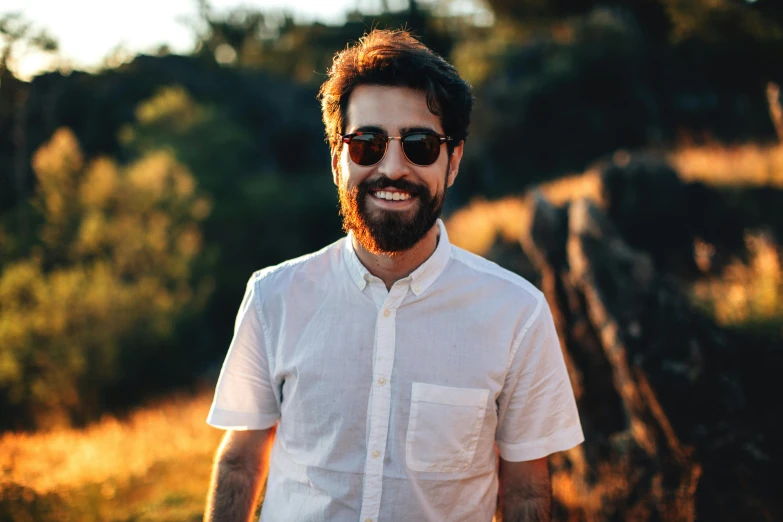 man with sunglasses smiling in field at sunset