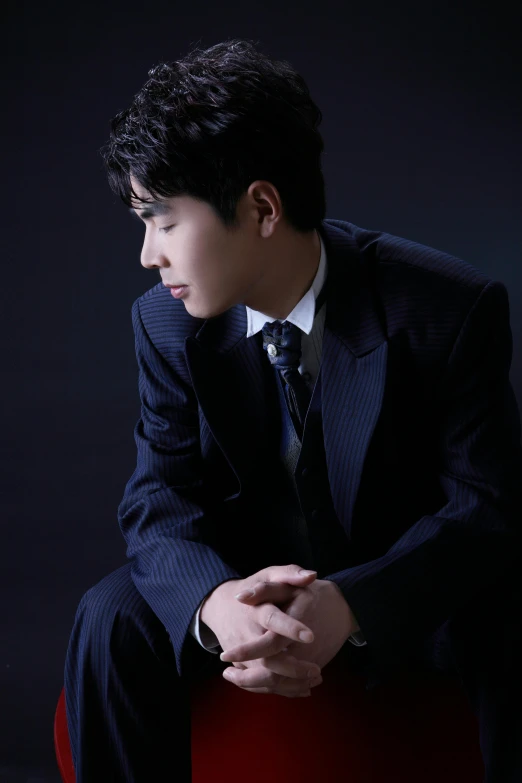 a man in a suit sitting on a red chair, an album cover, inspired by Zhang Han, elegant profile pose, yuya nagai, portrait n - 9, ap