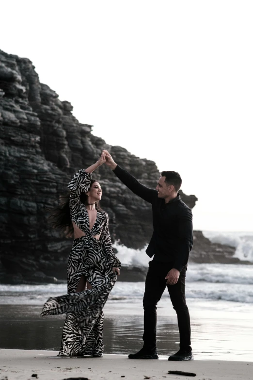 a man and a woman dancing on a beach, on a dark rock background, brooke ashling, coastal, flowy