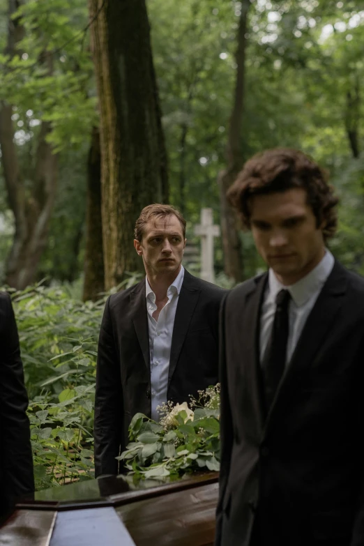 a group of men standing next to each other in a forest, man in black suit, dreaming bodies, warsaw, flowers around