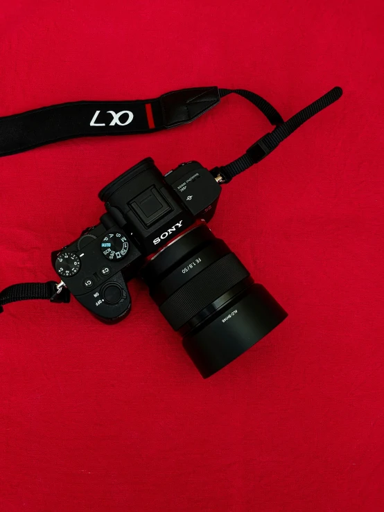 a camera sitting on top of a red surface, by Adam Marczyński, sony a7, black and red silk clothing, plushie photography, no - text no - logo