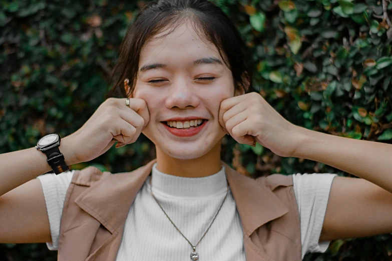 a woman standing in front of a bush with her hands on her ears, inspired by Kim Jeong-hui, trending on pexels, smile with large front teeth, portrait of a japanese teen, background image, smiling down from above