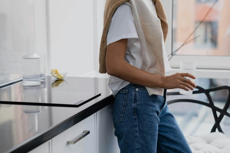 a woman standing in a kitchen next to a window, by Nina Hamnett, trending on pexels, happening, outfit : jeans and white vest, coffee stain on napkin, at the counter, angled