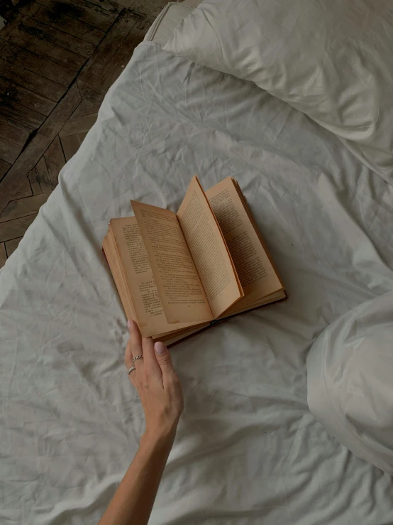 a hand on a white bed reading a book