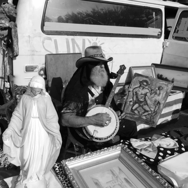 a black and white photo of a man playing a banjo, a black and white photo, by Otis Kaye, pexels, funk art, selling his wares, an arcylic art, belongings strewn about, christian saint