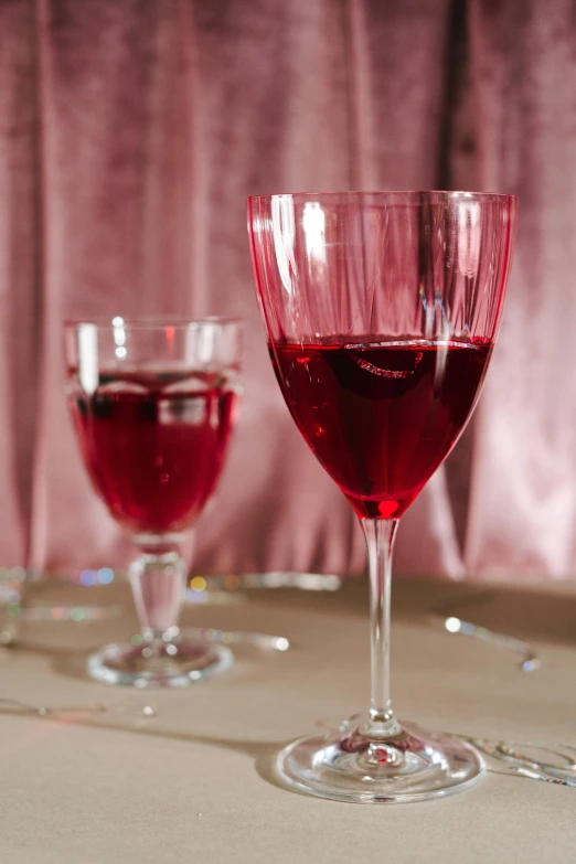 two wine glasses on a table with a pink background