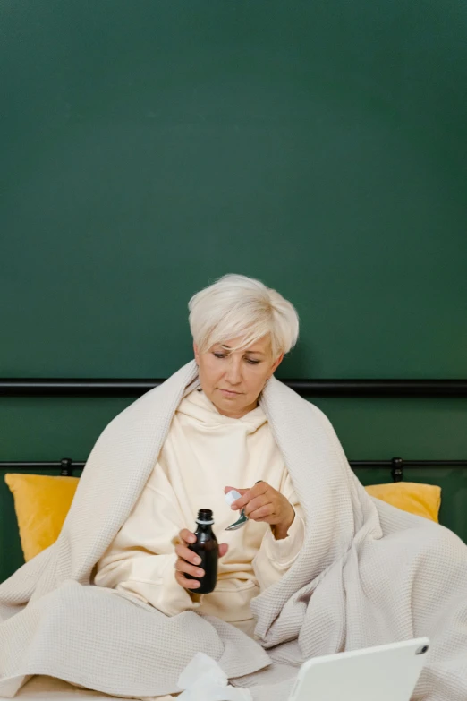 a woman sitting on a bed with a bottle of soda, pexels, a silver haired mad, dressed in a green robe, medical, square