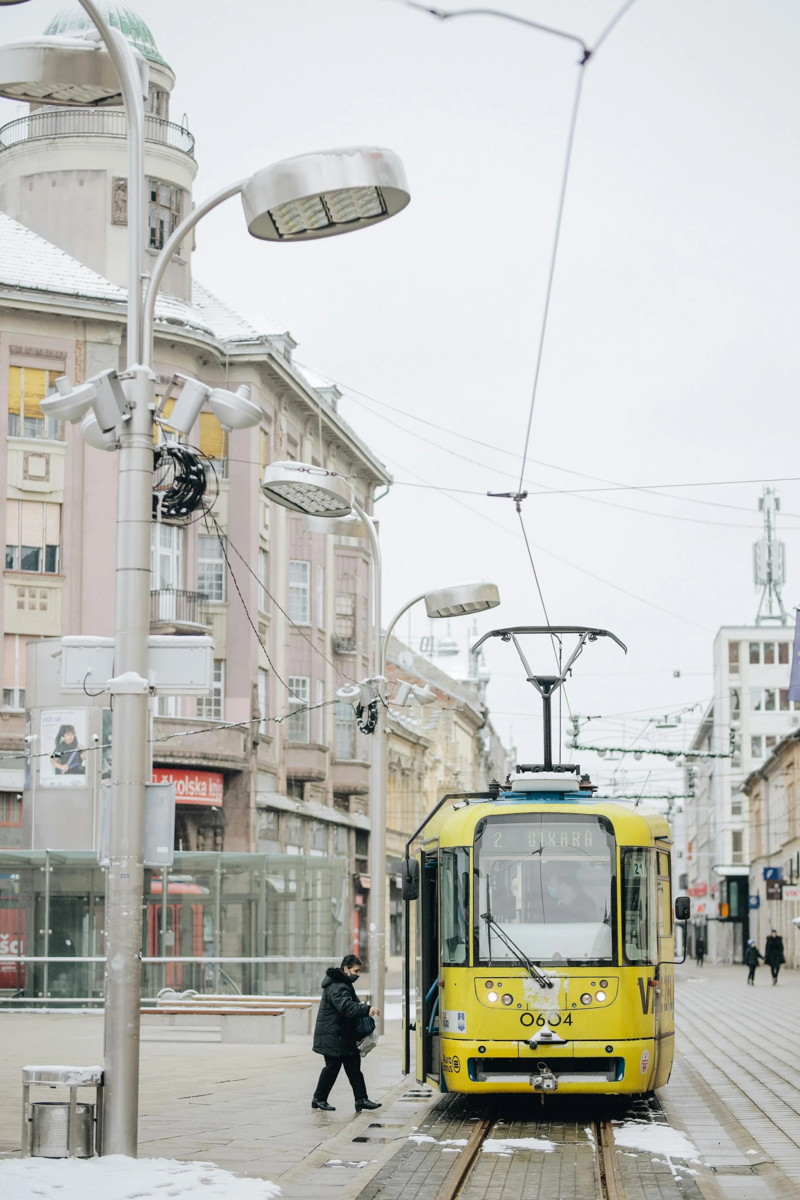 a yellow train traveling down train tracks next to tall buildings, inspired by Ernő Tibor, street tram, winter vibes, silver and yellow color scheme, shops