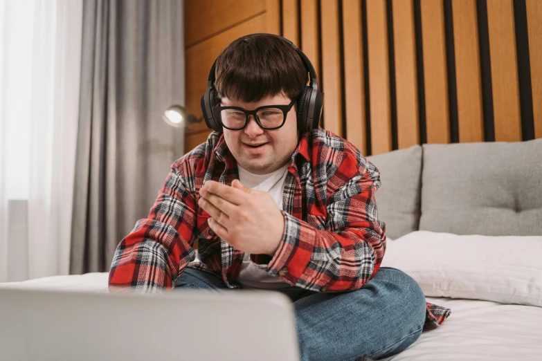 a man sitting on a bed with a laptop and headphones, trending on pexels, andy milonakis, chris farley, on a checkered floor, jewish young man with glasses