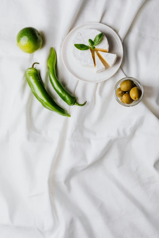 a close up of a plate of food on a bed, a still life, inspired by Ceferí Olivé, trending on unsplash, white splendid fabric, pickle, pepper, background image