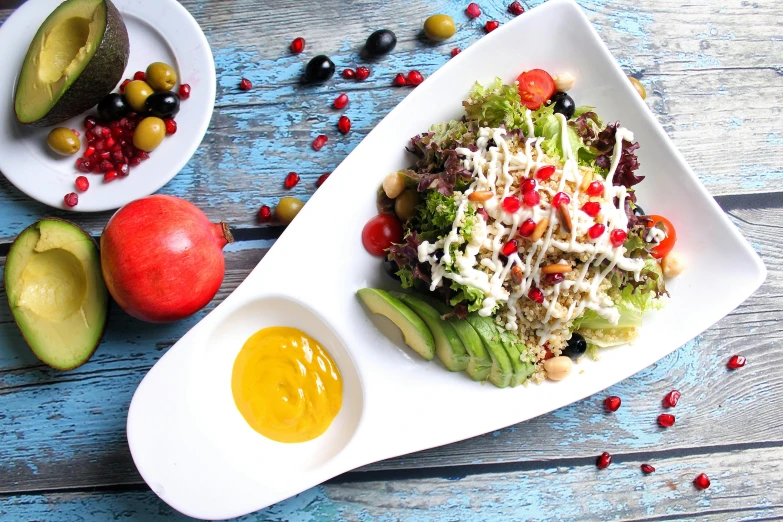 a white plate topped with a salad next to an avocado, by Julia Pishtar, unsplash, pomegranade, square, daily specials, russian and japanese mix