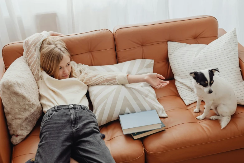 a woman laying on a couch next to a dog, a cartoon, trending on pexels, leather couch, lonely family, with small cat on lap, teenager hangout spot