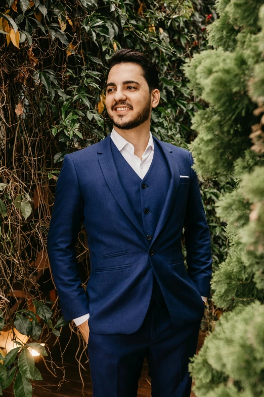 a man in a blue suit standing in a garden, an album cover, inspired by Ramon Pichot, pexels contest winner, three piece suit, sayem reza, elegant smiling pose, looking from side!